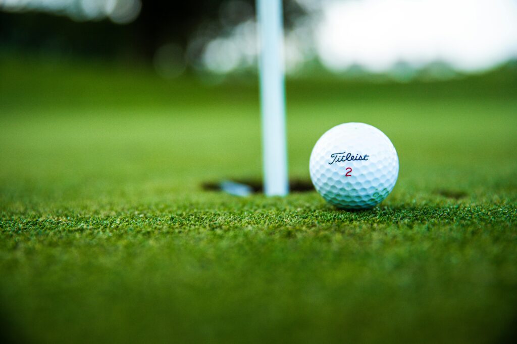 Close-up view of a Titleist golf ball on the green, inches away from the hole, capturing the essence of precision and skill.